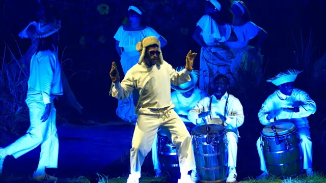 Artista puertorriqueño Bad Bunny en el escenario, con ropa blanca y músicos detrás