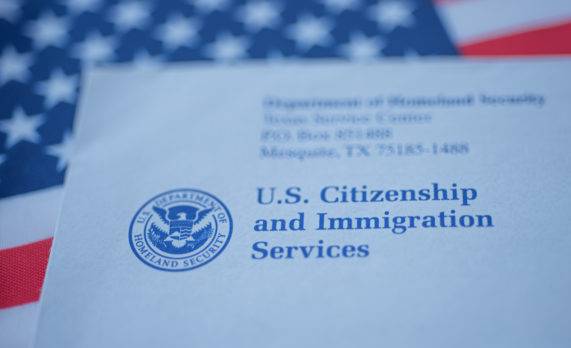 Mano tocando la carta (sobre) de USCIS sobre el fondo de la bandera de Estados Unidos.