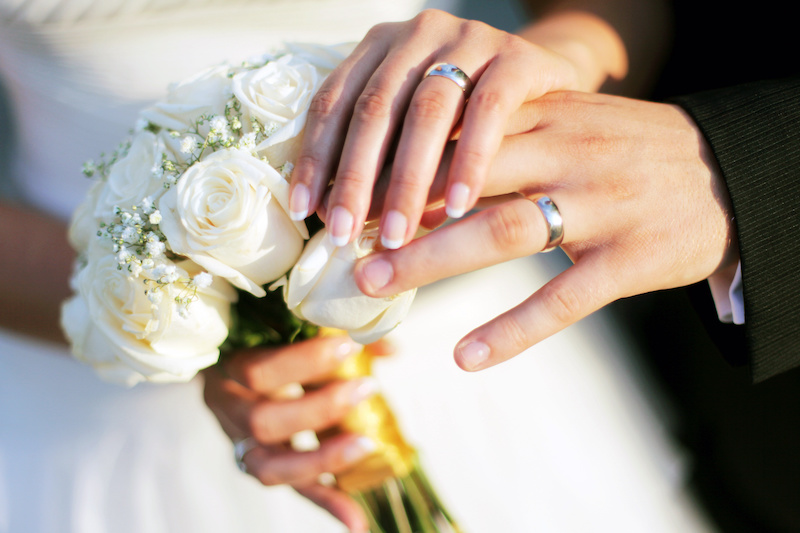 Anillos de boda, ramo y manos sosteniendo