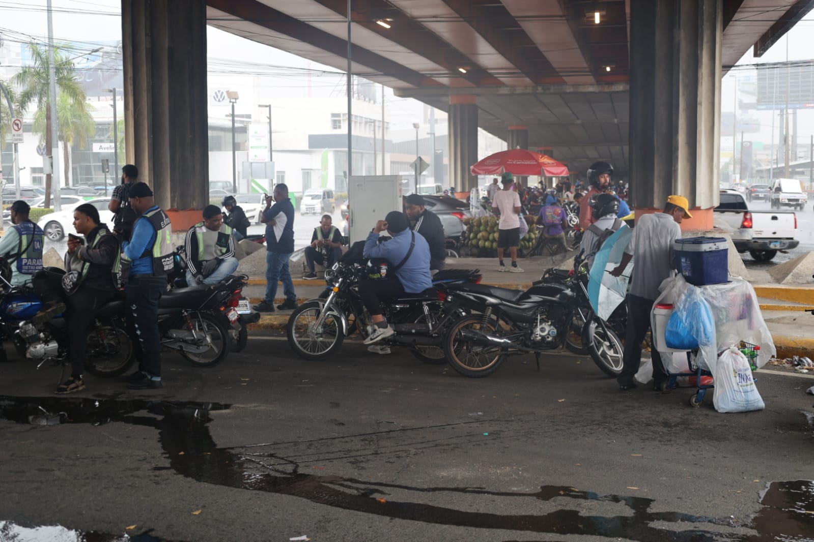 Automovilistas y ciudadanos se resguardan de la lluvia bajo la elevada avenida John F. Kennedy durante los aguaceros registrados este sábado en Santo Domingo. Foto: Guillermo Burgos.