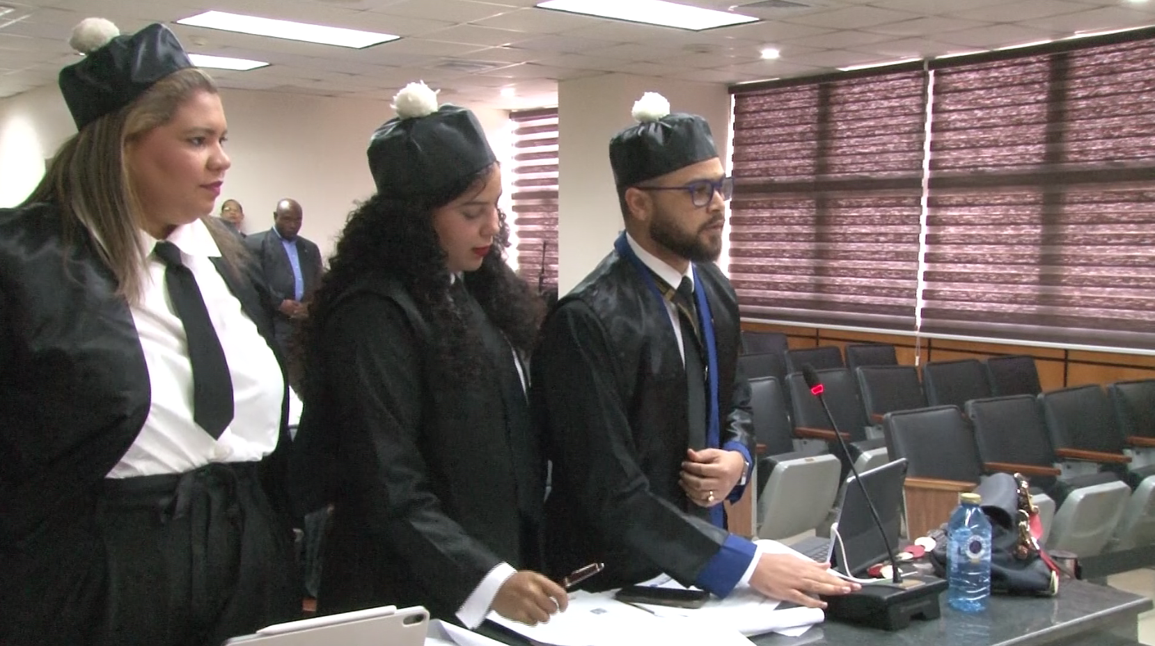 Abogados vestidos con togas durante una audiencia en una sala con micrófonos y asientos