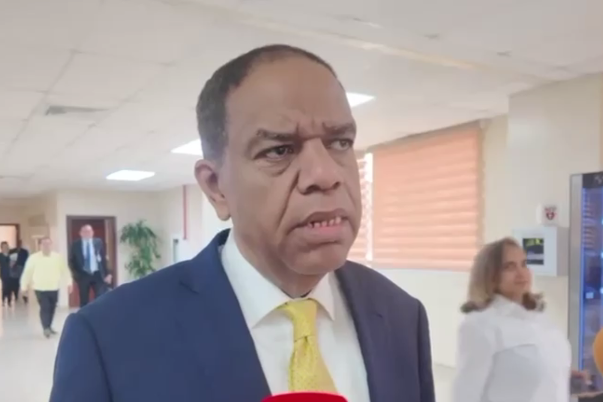 Hombre de traje y corbata amarilla ofrece declaraciones a la prensa en un pasillo institucional