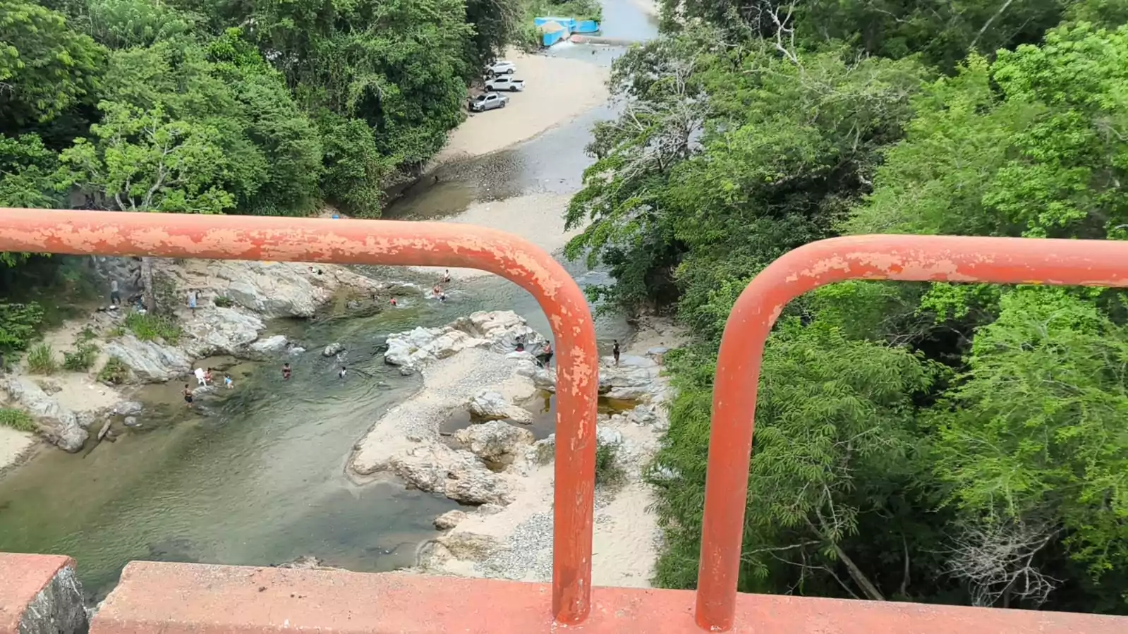 Río entre rocas y vegetación visto desde un puente, con gente bañándose en la corriente