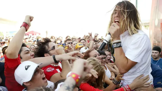 Jared Leto, vocalista de Thirty Seconds to Mars, actuando al aire libre ante una multitud que se abalanza hacia él. Canta frente a un micrófono y su cabello le cae sobre el rostro (Foto de J. Shearer/WireImage).