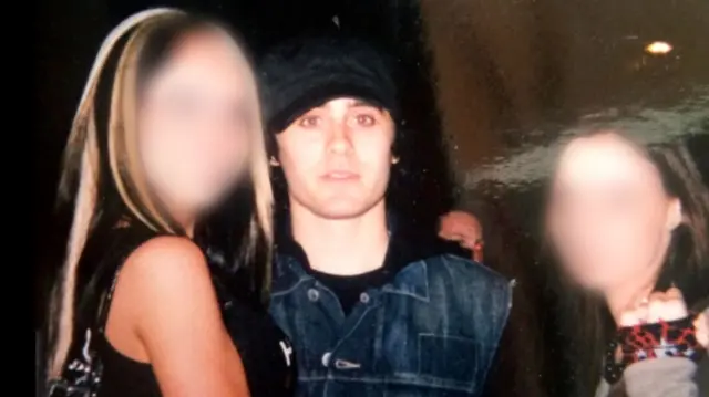 Jared Leto, con una chaqueta vaquera y un sombrero negro, mira fijamente a la cámara mientras posa con dos niñas cuyos rostros hemos difuminado. 
