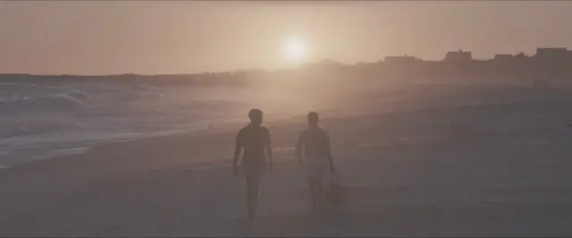 Fotograma del documental Bring Me The Beauties en el que se ve a dos personas caminando en una playa. Hay una suerte de neblina.