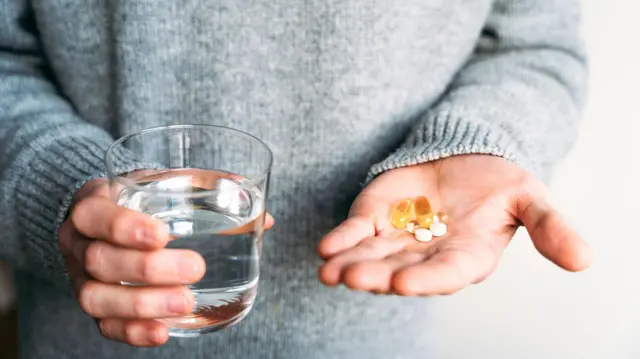 Una persona tiene varias pastillas en una mano y un vaso de agua en la otra.