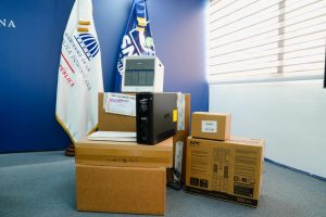Cajas con equipos electrónicos junto a banderas institucionales en una oficina
