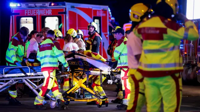 Varios miembros del personal de los servicios de emergencia se encuentran cerca de una ambulancia, con una persona en una camilla.