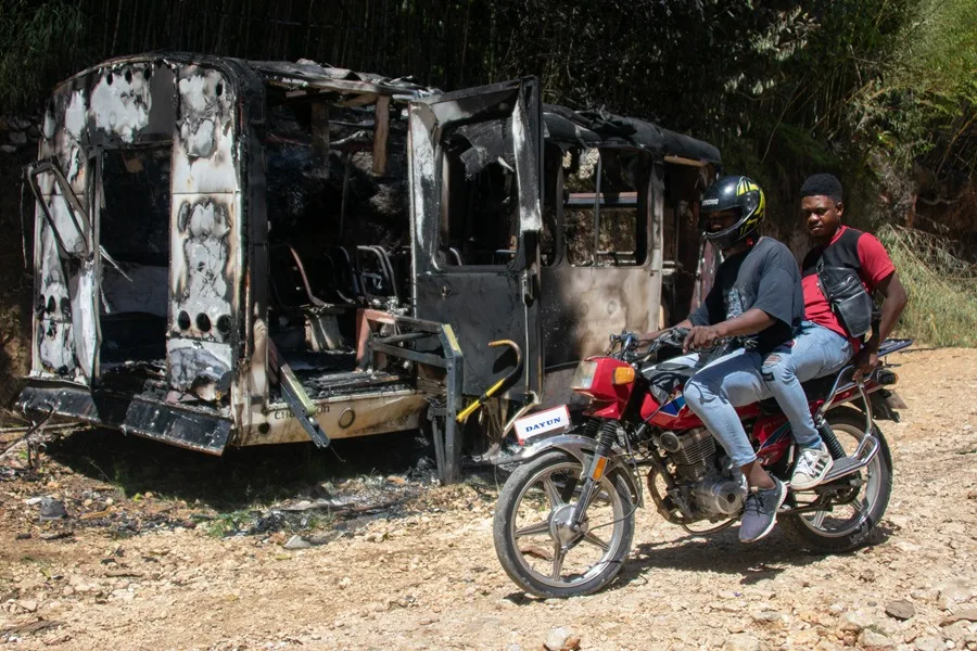 Personas en motos cruzan junto a un vehículo quemado este lunes, en el sector de Kenscoff (Haití). EFE
