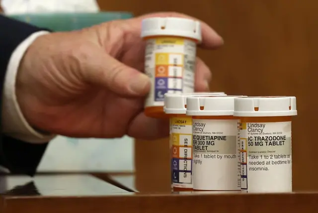 Una mano sostiene un frasco de medicina, las otras dos están sobre una mesa.