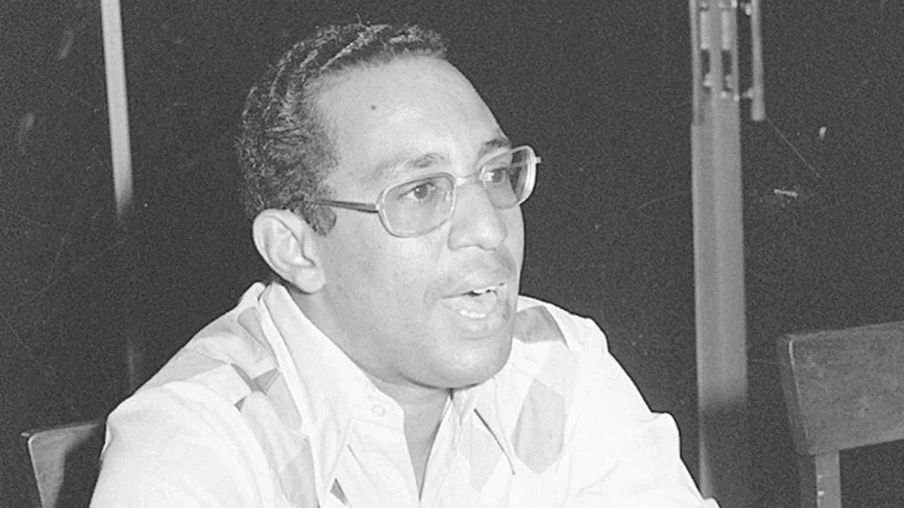 Hombre con gafas habla durante una entrevista o reunión, en una fotografía en blanco y negro
