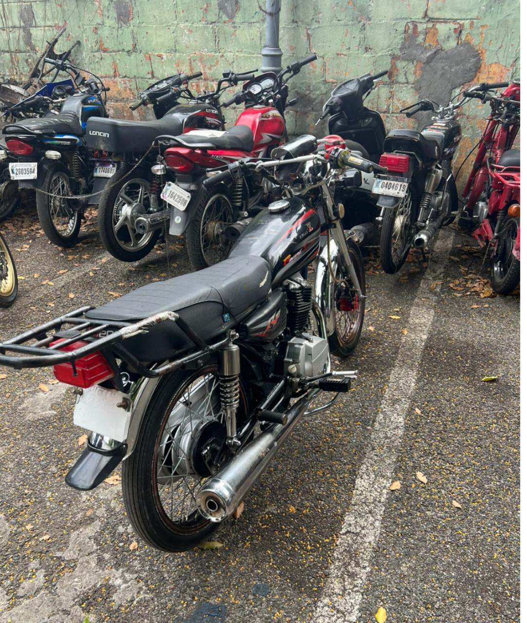Motos estacionadas en un lote, alineadas junto a un muro deteriorado