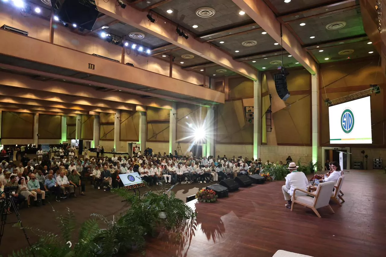 Auditorio lleno durante un evento del SID con panelistas en escenario y pantalla con el logo institucional
