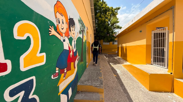 Pasillo del centro educativo con mural infantil y una persona caminando entre edificios pintados de amarillo
