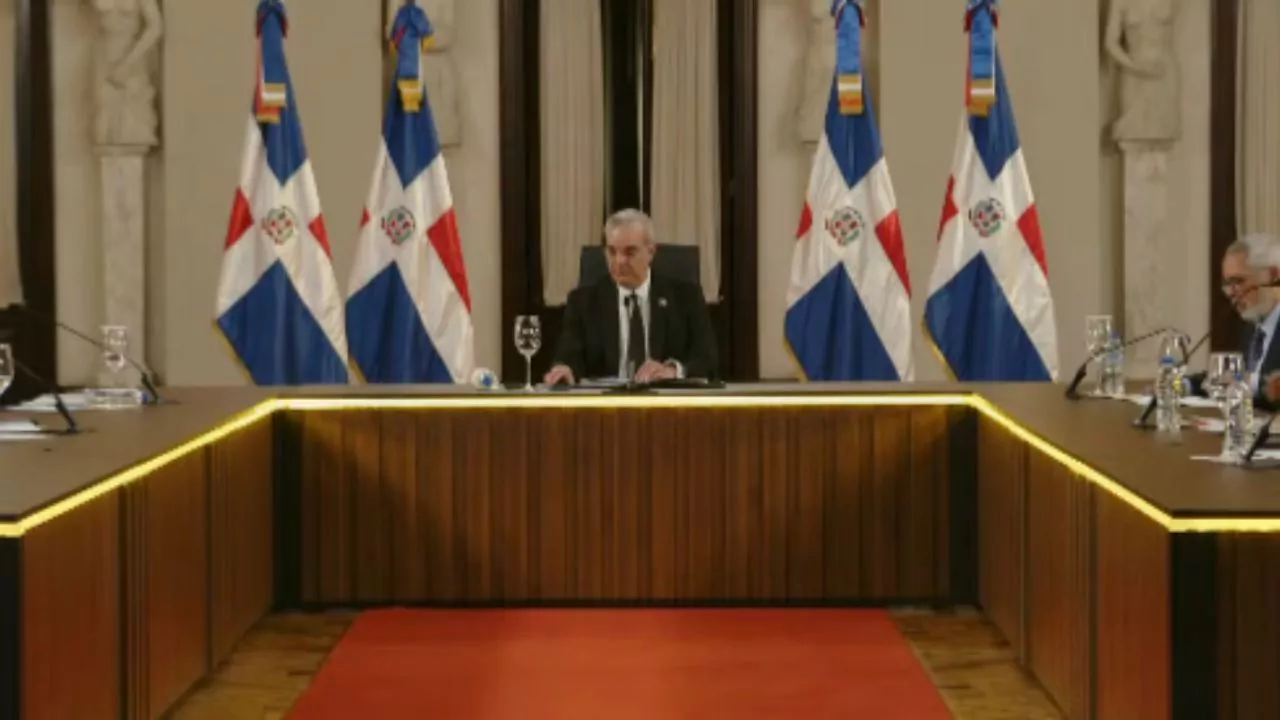 Funcionario encabeza reunión oficial con banderas de República Dominicana en salón de gobierno