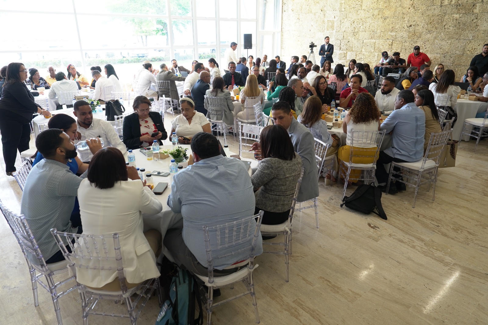 Los asistentes participan en una reunión con mesas redondas en una gran sala durante una actividad informativa