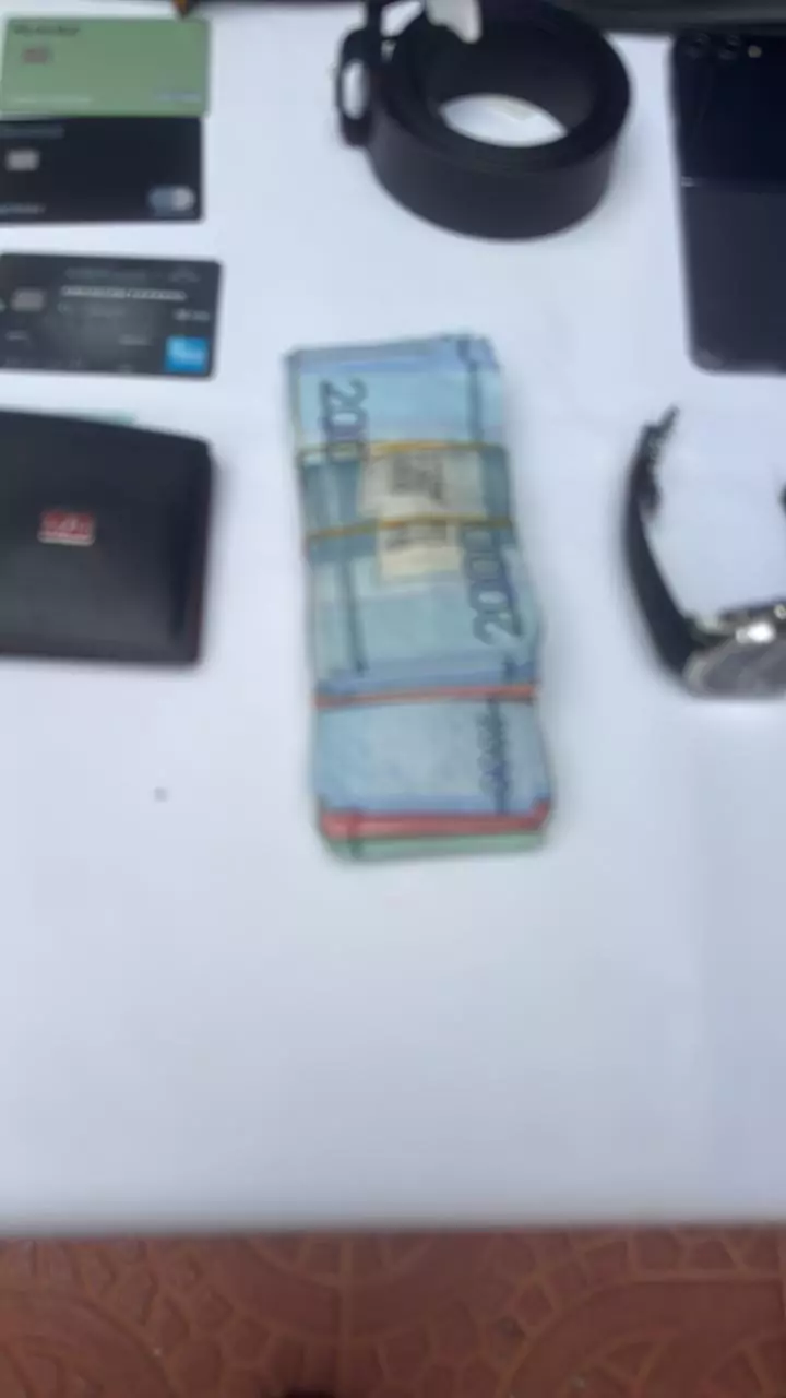 Efectivo, tarjetas bancarias, teléfono celular, reloj y billetera sobre una mesa blanca en posible incautación
