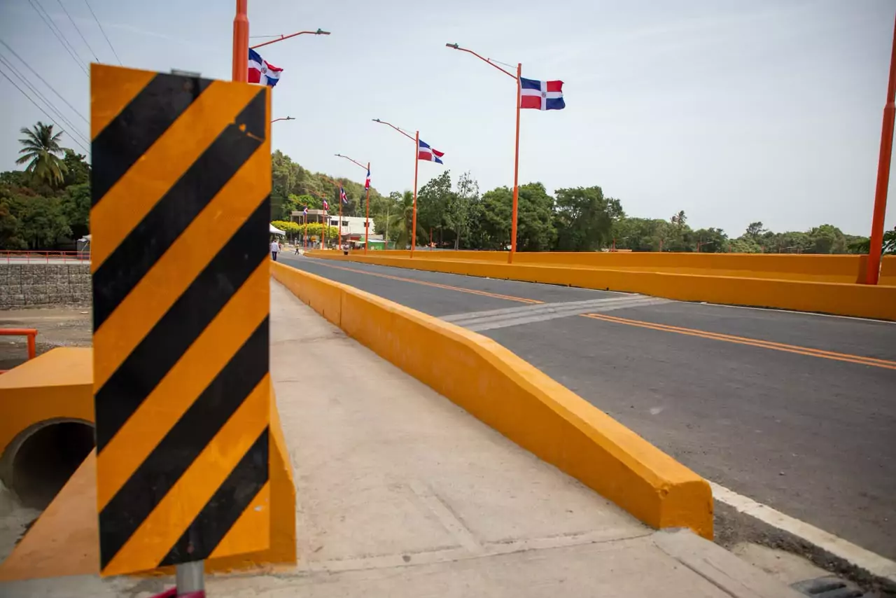 Puente de Los Hierros en Baní tras su inauguración, con nueva calzada asfaltada, barandillas amarillas y banderas dominicanas