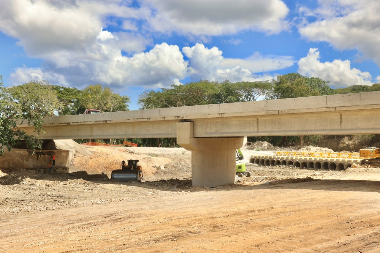 Puente de hormigón en construcción sobre suelo seco, con maquinaria y tuberías en una obra vial