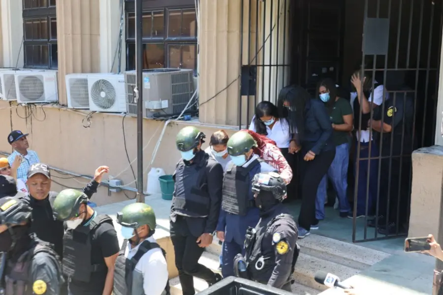 Agentes escoltan a varias personas a la salida de un edificio oficial durante un operativo judicial en República Dominicana
