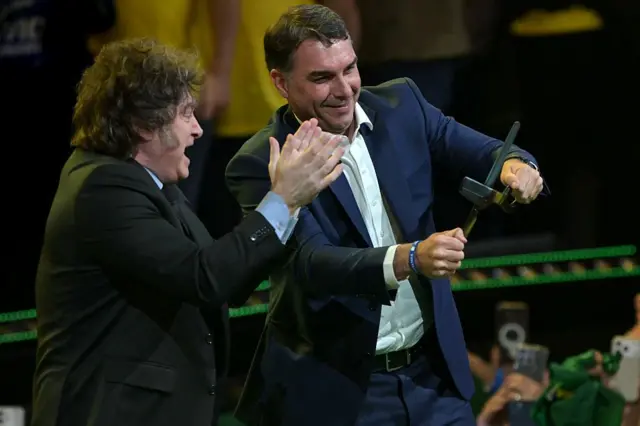 El presidente de Argentina, Javier Milei, aplaude mientras el candidato presidencial de derecha de Brasil, Flavio Bolsonaro, sostiene unas tijeras gigantes durante su presentación de candidatura en la convención del Partido Liberal en São Paulo, Brasil, el 25 de julio de 2026.