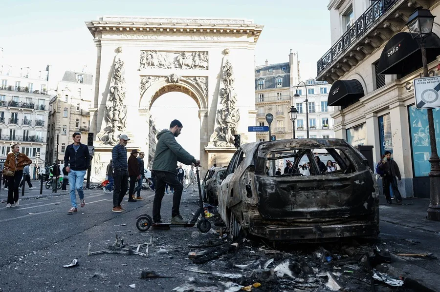 La gente pasa junto a un coche quemado tras los enfrentamientos entre la policía antidisturbios y los manifestantes en París, Francia. EFE/EPA/MOHAMMED BADRA