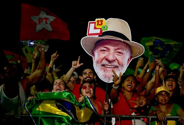 Simpatizantes de Lula muestran una imagen con el rostro del presidente brasileño y banderas de Brasil y del Partido de los Trabajadores durante un evento político en Río de Janeiro el 18 de octubre de 2026.