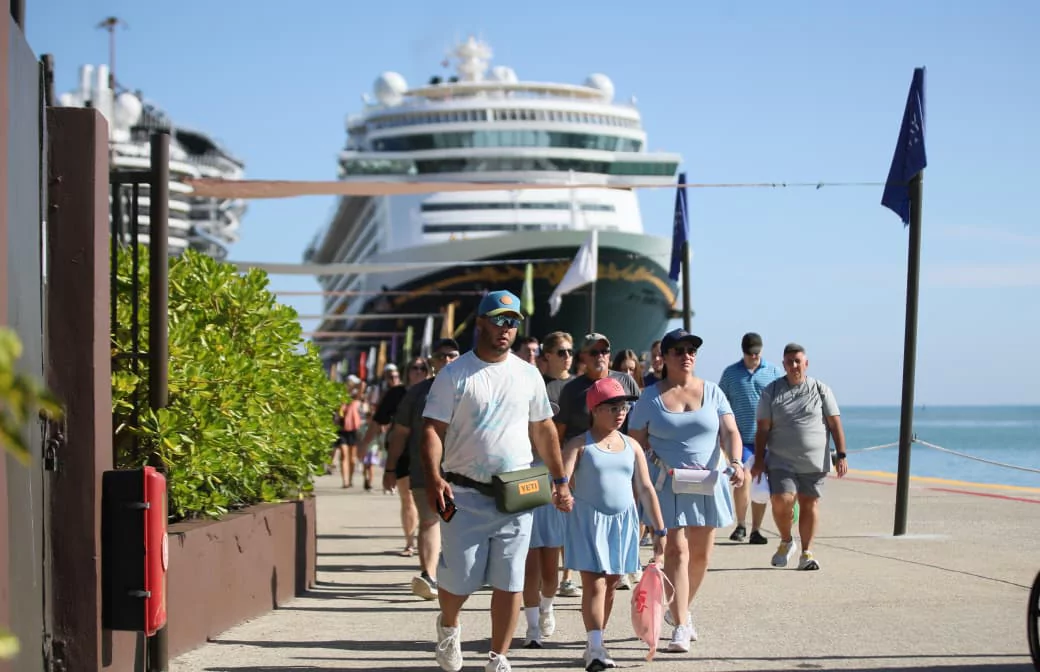 Turistas caminan junto a un crucero atracado en un muelle, en un escenario vinculado al turismo marítimo.