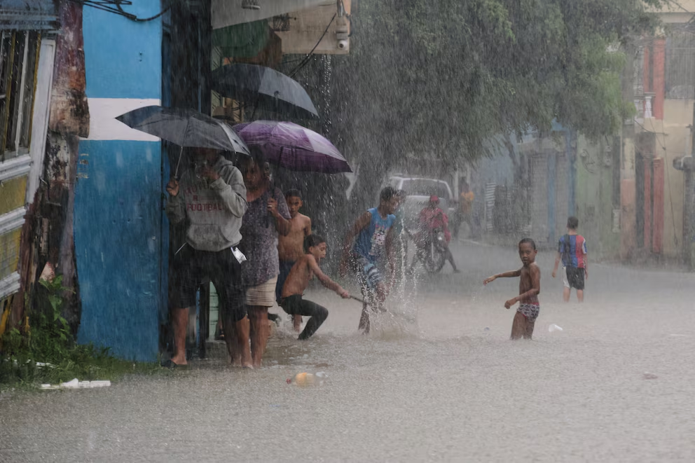 Niños y adultos bajo fuertes lluvias en una calle inundada en República Dominicana, un riesgo climático que afecta su salud y educación