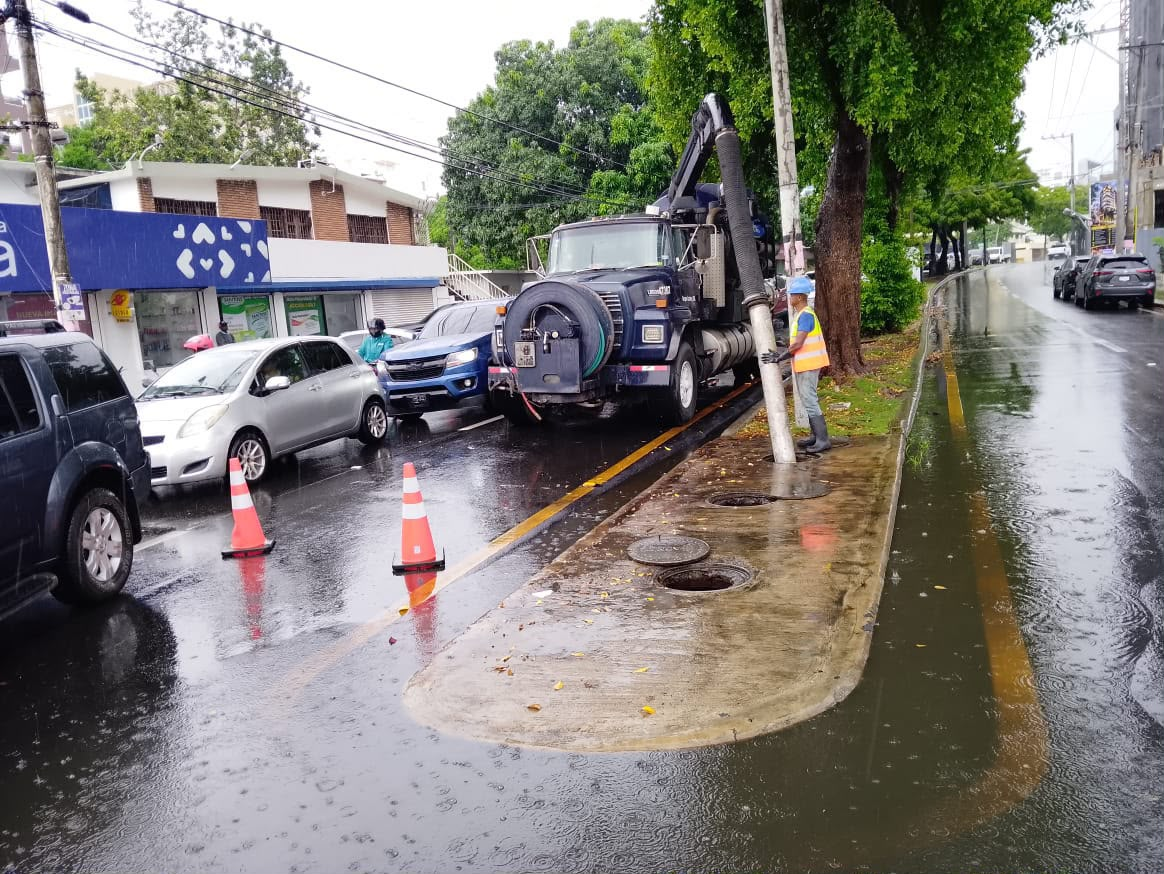 Camión aspirador y trabajador destapan drenaje pluvial en calle inundada en Santo Domingo por las lluvias
