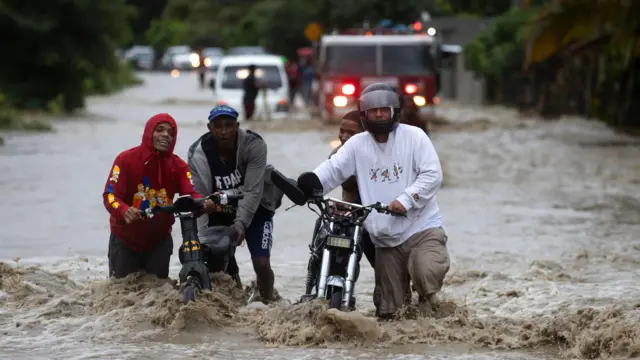 Vecinos empujan motocicletas por calles inundadas en República Dominicana tras fuertes lluvias