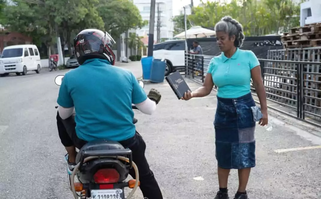 Una mujer le entrega una Biblia a un automovilista en una calle del Distrito Nacional durante un día de la Iglesia Adventista.